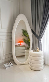 Modern interior with a large oval mirror, white stool, and decorative items.