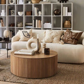 Modern living room with a white sofa, round wooden coffee table, and bookshelf.