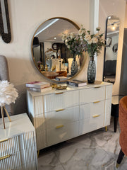 Decorative dresser with round mirror, flowers, and books in a stylish room.