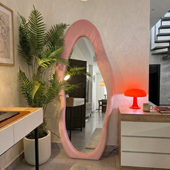Pink oval mirror in a modern living room with plants and furniture.