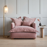 Pink armchair with cushions in a room with a light gray wall and wooden floor.