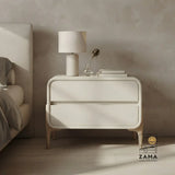 Modern minimalist white bedside table with rounded edges and wood base, positioned on the right side of a styled bedroom next to a bed