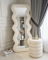 Decorative mirror with wavy design in a room with a shelf and curtains.