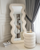 Decorative mirror with wavy design in a room with a shelf and curtains.