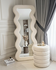 Decorative mirror with wavy design in a room with a shelf and curtains.