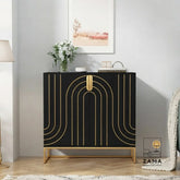 A modern, black wooden buffet console with geometric gold arch patterns and an elevated gold base, styled in an elegant living room with a vase of flowers and framed art on top. Logo for Zama Home Store in the corner.