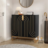 A sophisticated black and gold geometric accent cabinet positioned in an entryway, featuring a table lamp, vintage radio, and mirror above it, with an umbrella stand nearby. Zama Home Store logo is present.