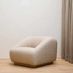 Beige textured armchair in a minimalistic room with a neutral wall and curtain.