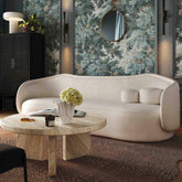 Modern living room with a white sofa, round wooden coffee table, and floral wall art.