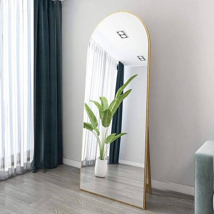 Full-length mirror with gold frame in a room with curtains and a plant.