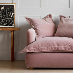 Pink sofa with decorative pillows in a room with a wooden side table and framed artwork on the wall.