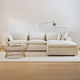 Beige sectional sofa in a modern living room with a coffee table and wall lamp.