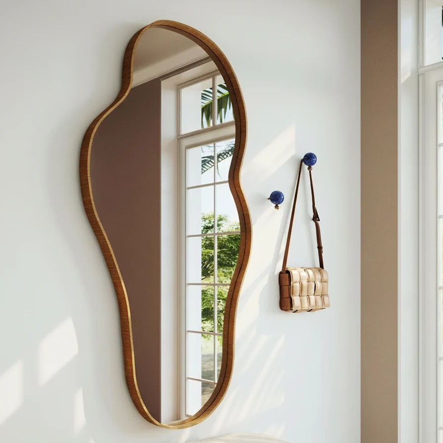 Elegant wavy mirror on a white wall with a bench and handbag in the foreground.