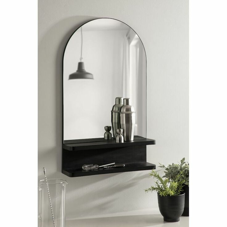 Wall mirror with a black shelf displaying decorative items against a light gray wall.