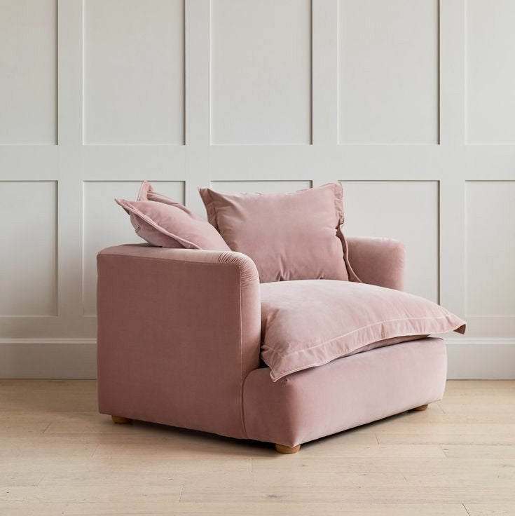 Pink armchair with cushions against a white paneled wall.