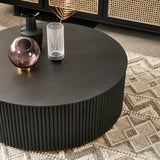 Round black coffee table with decorative items in a living room setting.