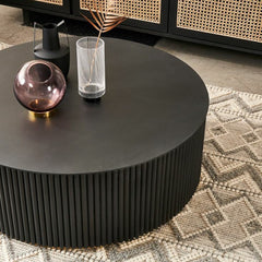Round black coffee table with decorative items in a living room setting.