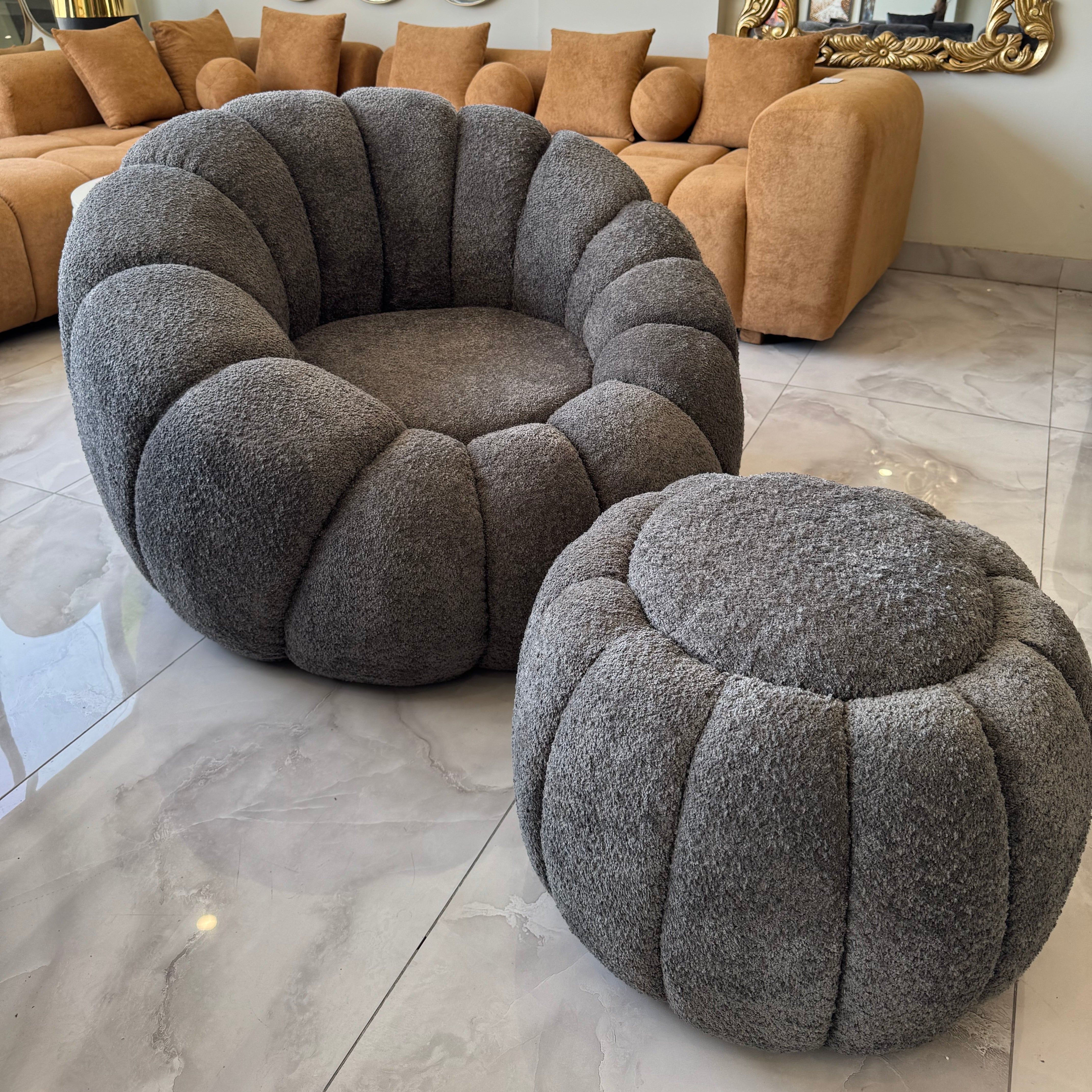 Gray textured armchair and ottoman in a living room setting with a beige sofa and decorative mirrors.