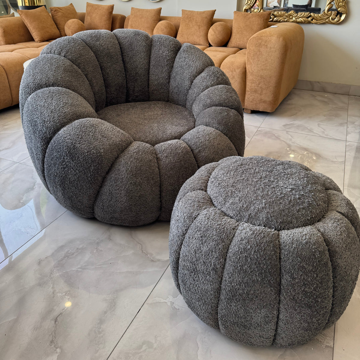 Gray textured armchair and ottoman in a living room setting with a beige sofa and decorative mirrors.