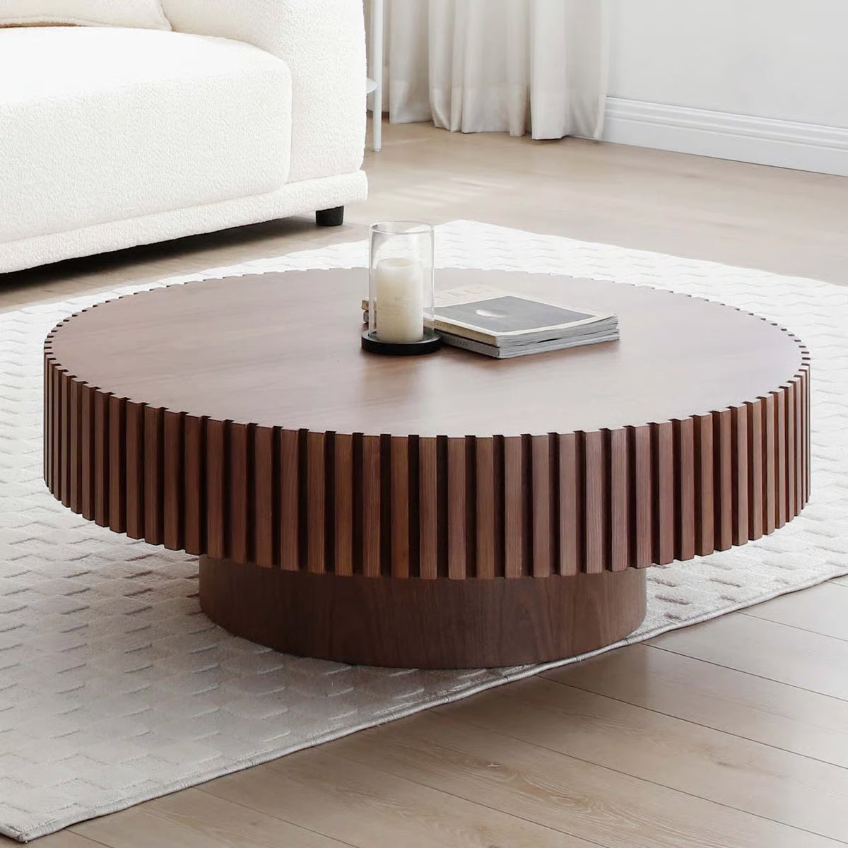 Round wooden coffee table in a living room setting with a candle and books on top.