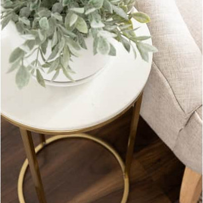 Small round white table with gold legs next to a beige sofa, topped with a green plant.