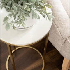 Small round white table with gold legs next to a beige sofa, topped with a green plant.