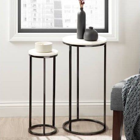 Two small round tables with black metal legs and white marble tops in a room with a window.