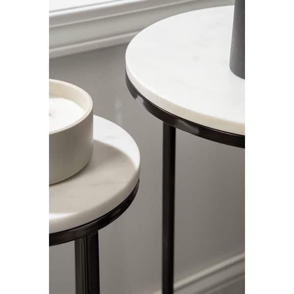 Two round side tables with white marble tops and black metal frames on a neutral background.