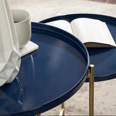 Navy blue round table with gold legs, white mug, and book on a light wooden floor.