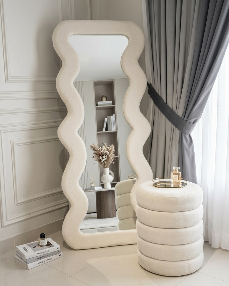 Decorative mirror with wavy design in a room with a shelf and curtains.