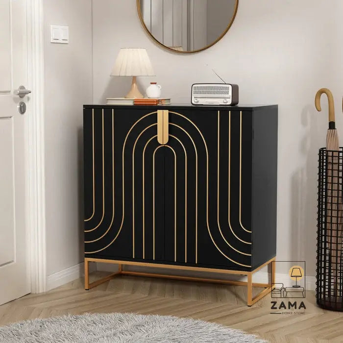 A sophisticated black and gold geometric accent cabinet positioned in an entryway, featuring a table lamp, vintage radio, and mirror above it, with an umbrella stand nearby. Zama Home Store logo is present.
