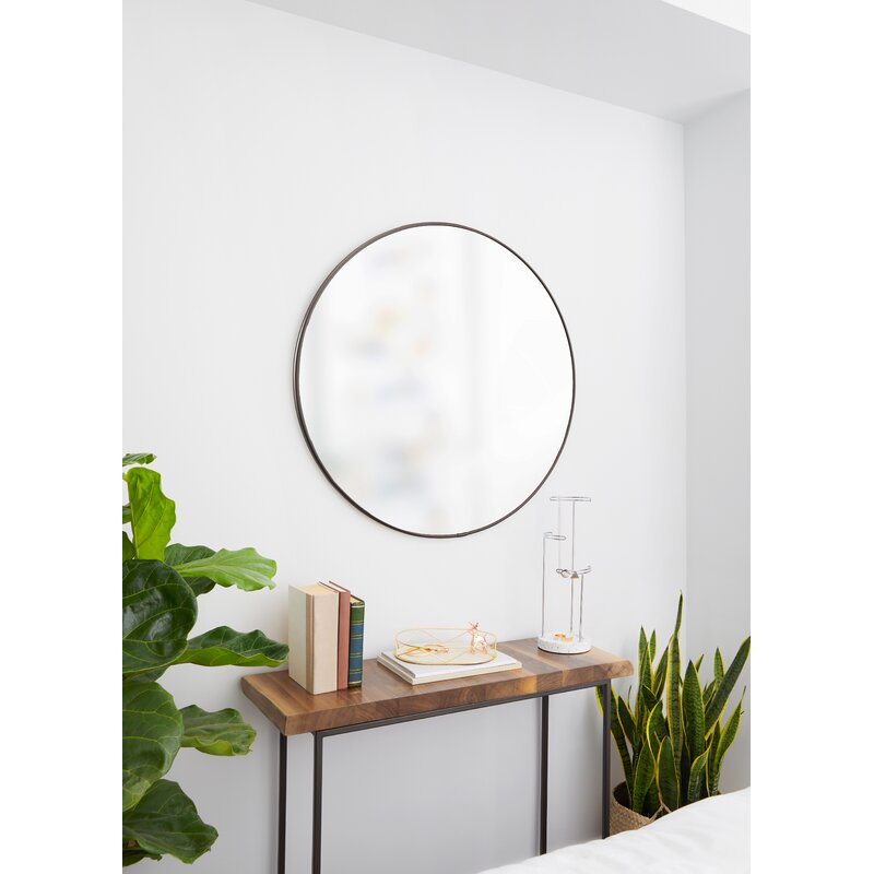 Round mirror on a white wall above a wooden console table with decorative items.