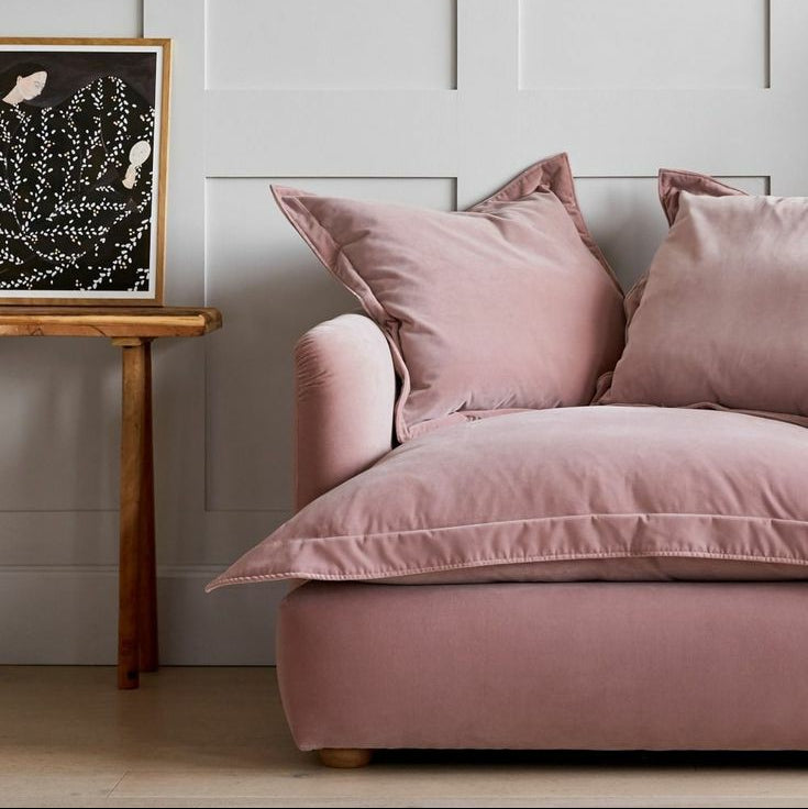 Pink sofa with decorative pillows in a room with a wooden side table and framed artwork on the wall.