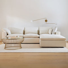 Beige sectional sofa in a modern living room with a coffee table and wall lamp.