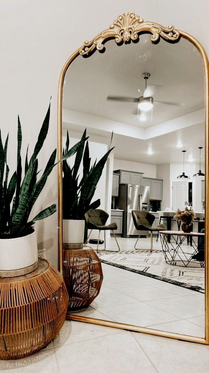 Large ornate mirror reflecting a modern kitchen with a wicker stool and potted plant.