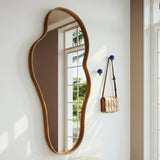 Elegant wavy mirror on a white wall with a bench and handbag in the foreground.