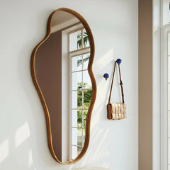 Elegant wavy mirror on a white wall with a bench and handbag in the foreground.