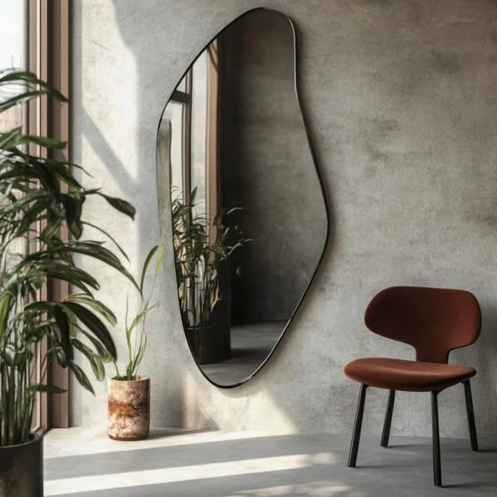 Modern interior with a large, wavy mirror on a textured wall, a red chair, and plants.