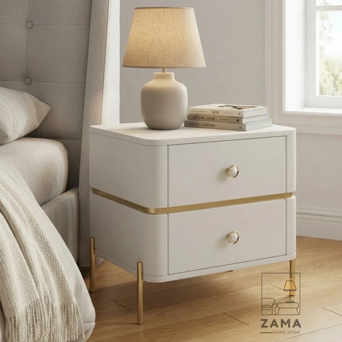 Modern white side table by Zama Home Store with gold legs beside a bed with a lamp